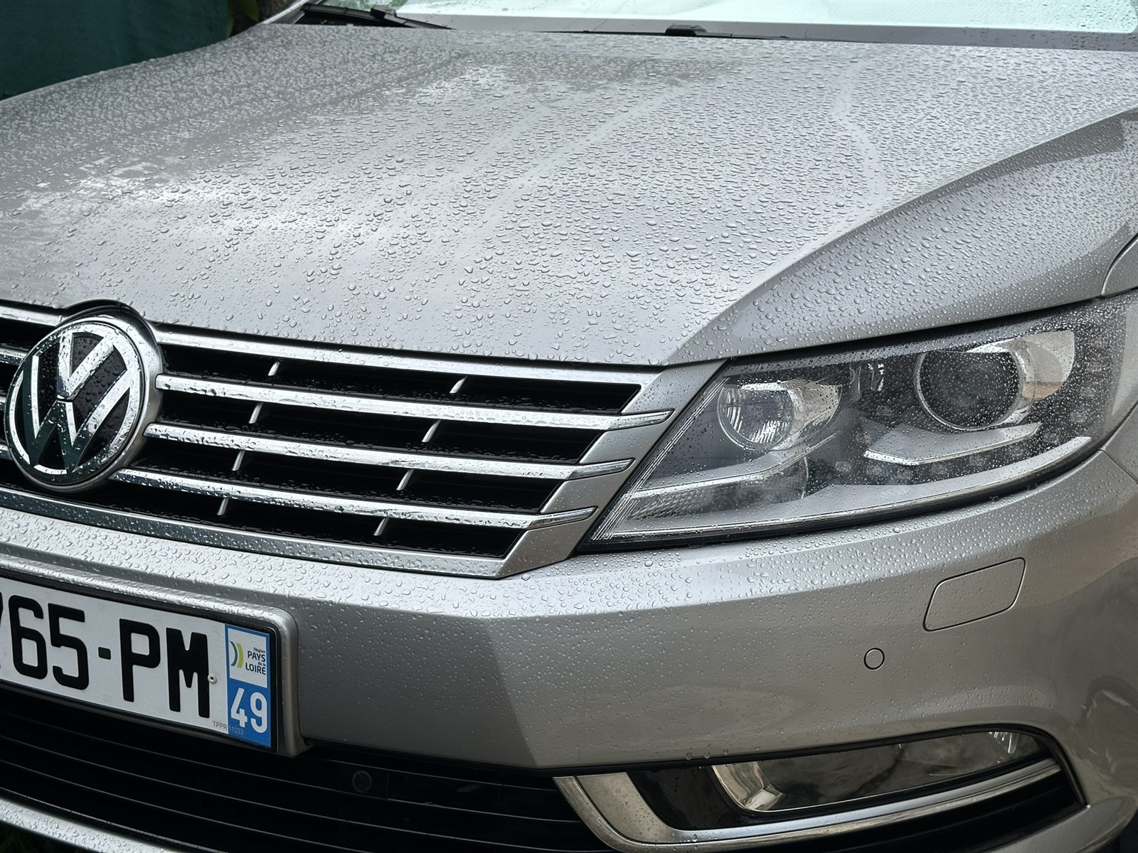 Gros plan sur la calandre et le phare avant du taxi gris, couverts de gouttes de pluie